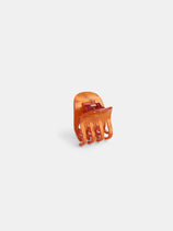 The Small Round Claw is an orange, translucent acetate hair accessory with curved prongs and a visible gold-coated metal spring, shown upright on a plain white background.