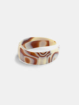 A wide, glossy headband handcrafted in France features a swirled pattern in shades of brown, cream, and beige, displayed on a plain white background.