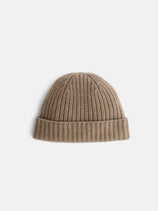 The Cashmere Beanie, featuring a beige ribbed knit design and a folded cuff, is displayed on a plain white background. This soft hat combines warmth with timeless style.