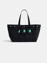 The Perfect Weekend Tote is a large black cotton bag with two handles, silver button accents, and green and white “JMW” letters on the front—ideal for monogram fans.