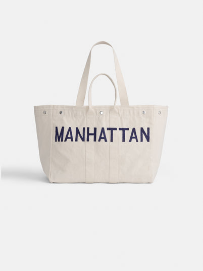 The Manhattan Painted Perfect Weekend Tote is a spacious off-white bag with dual handles and “MANHATTAN” in bold navy blue on the front—an ideal custom-made, stylish accessory.