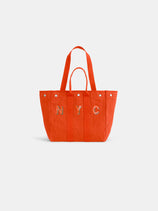 The Painted Perfect Weekday Tote is a bright orange bag with two handles, NYC embroidery on one side, a structured shape, and silver snap buttons along the top edge.