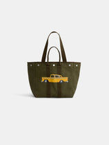 The Limited Edition Painted Perfect Weekday Taxi Tote is a green canvas bag with dark handles, showcasing an embroidered yellow cab and checkered stripe on the front. Inspired by Brooklyn artists, it features eye-catching silver button accents.