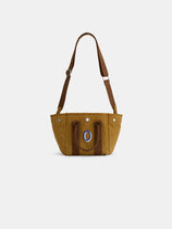 The Mini is a brown cotton canvas tote bag featuring dual short handles, an adjustable shoulder strap, and a blue oval logo on the front, shown against a plain white background.