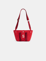 The Mini is a red canvas shoulder bag with an adjustable strap, two short handles, and a bold white letter S on the front. Metal rivet accents add style. The personalized tote is shown against a plain white background.