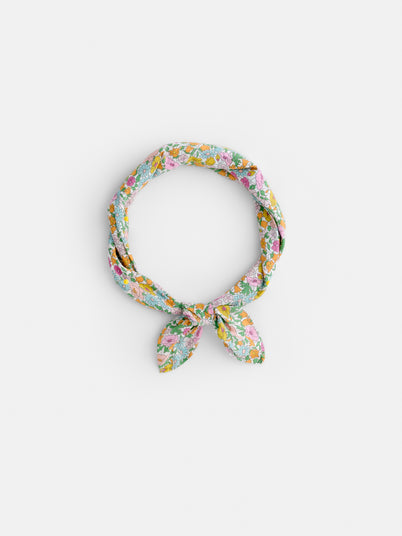 The Alex Mill x Liberty Bandana, a light blue floral scarf made from 100% cotton with pink, yellow, and green patterns, is tied in a loose knot on a white background—perfect for summer.