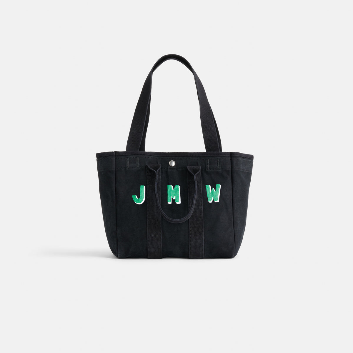 The Painted Perfect Daily Tote is a black bag with two handles, featuring the initials JMW in green and white on the front, shown against a plain white background.