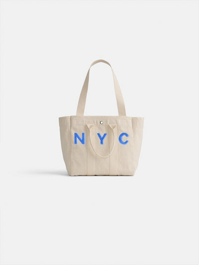 The Perfect Daily Tote is a beige cotton bag with two handles and bold blue “NYC” lettering on the front, shown against a white backdrop. It's a stylish and practical choice for everyday use.
