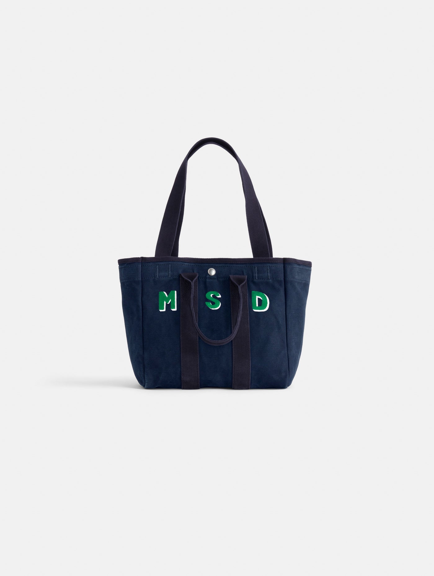 The Painted Perfect Daily Tote is a navy blue bag with two handles, featuring the initials MSD in green and white on the front, shown against a plain white background.