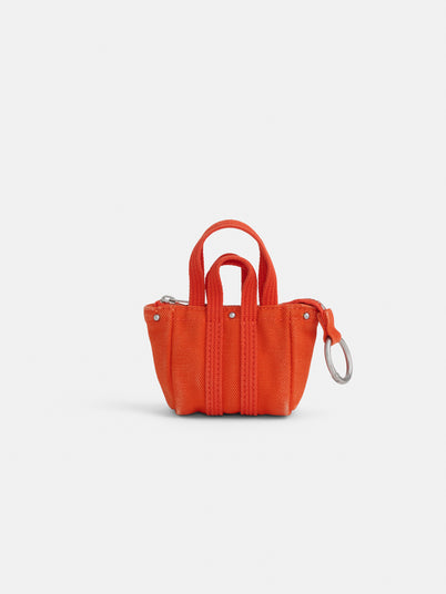 The Teeny Tiny Tote Keychain is a small, bright orange miniature tote bag with two short handles and a zipper closure, photographed on a white background. A functional silver keychain is attached to one side of the bag.