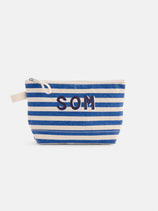 The Painted Perfect Striped Canvas Pouch features blue and white horizontal stripes, bold navy SOM letters on the front, and a beige fabric zipper pull.
