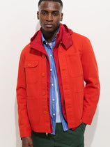 A man stands against a plain white background, wearing the Garment Dyed Work Jacket In Recycled Denim over a blue and white striped shirt. His expression is neutral, with his left hand in his jacket pocket.