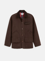 The Frontier Jacket In Canvas is a dark brown 1950s-style barn jacket featuring a corduroy collar, button closure, three front flap pockets, and plaid flannel lining at the neckline, shown on a white background.