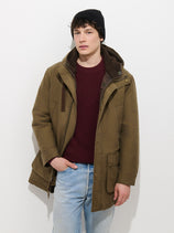Man wearing an Ashby Parka in Vintage Twill, a brown hooded parka with a sherpa-lined hood, over a burgundy sweater and light blue jeans.