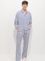 A person stands against a plain white background, wearing The Striped Waffle Pant—navy blue and white horizontal stripes with red accents—and has their hands tucked in the pants' pockets.