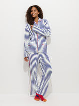 A woman stands against a plain white background, smiling and looking slightly to the side. She wears The Striped Waffle Pant with red piping, paired with orange and red socks.