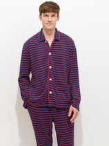 A person smiles at the camera against a plain white background, wearing The Striped Waffle Sleeping Shirt—navy blue and red striped 100% cotton pajamas with white buttons.