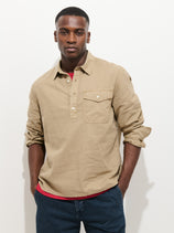 A man with a neutral expression stands against a white background, wearing the Carter Popover In Cotton Linen over a red T-shirt and blue jeans, his hands tucked into his pockets.