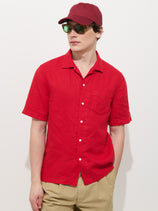 A person wears the Camp Shirt In Linen (red), beige pants, a red cap, and reflective sunglasses, standing against a plain white background with one hand in their pocket.