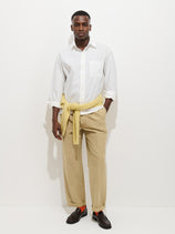 A man stands against a white background wearing the Franklin Shirt in Cotton Poplin, khaki pants, brown loafers, orange socks, and a yellow sweater tied around his waist.