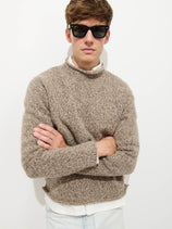 A man in dark sunglasses and a Marled Rollneck In Merino Wool, layered over a white shirt, stands with arms crossed against a plain white background.