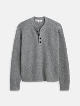 The Waffle Henley In Cashmere is a gray, long-sleeve sweater with a round neck and four black buttons on the placket. This soft waffle-knit cashmere style is shown laid flat against a white background.