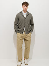 A young man stands against a white background, wearing the Alain Blazer In Cotton Linen over a white shirt, beige trousers, and white sneakers. His hands are in his pockets and he has a neutral expression.