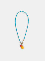 The Roxanne Assoulin Happy Cord Charm Necklace features a blue puffy heart, colorful cording with yellow accents, and two detachable charms—a yellow heart and a red bead—displayed on a white background.