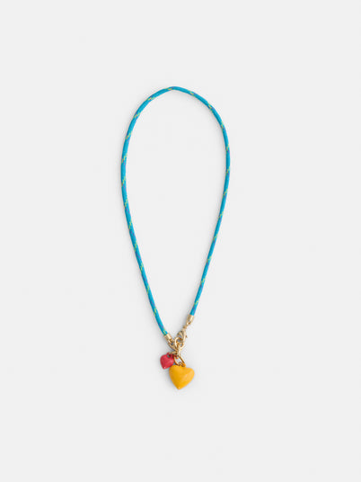 The Roxanne Assoulin Happy Cord Charm Necklace features a blue puffy heart, colorful cording with yellow accents, and two detachable charms—a yellow heart and a red bead—displayed on a white background.