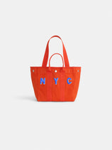 The Perfect Daily Tote: a bright orange cotton bag with two handles and blue "NYC" lettering outlined in white on the front, ideal for monogramming. Shown against a plain white background.
