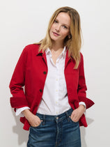 A woman with straight blonde hair wears the Britt Work Jacket in herringbone over a white button-up shirt and blue jeans, standing against a plain white background with her hands in her pockets, looking slightly to the side.