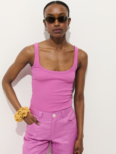 A person in sunglasses wears the 365 Ribbed Tank in pink and pink pants, stands against a white background, with a yellow scrunchie on their wrist and one hand in their pocket.