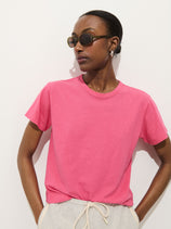 A person wearing round sunglasses, the Garcon Tee In Linen Cotton in bright pink, and light gray drawstring pants stands against a plain white background, looking to the side.