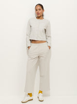 A woman stands against a white background wearing a light gray cotton double jersey long-sleeve buttoned top and matching Coco Sport Pant, paired with yellow socks, white sneakers, and her hands in her pockets for an effortless designer look.