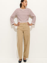 A woman stands against a plain white background wearing the 9th Street Pant—high-waisted cotton barrel leg pants with a detachable belt—paired with a red and white striped long-sleeve shirt, black flats, and earrings. Her hair is pulled back, hands on hips.