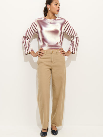A woman stands against a plain white background wearing the 9th Street Pant—high-waisted cotton barrel leg pants with a detachable belt—paired with a red and white striped long-sleeve shirt, black flats, and earrings. Her hair is pulled back, hands on hips.