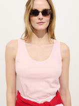 A woman with light brown hair wears sunglasses and the Garcon Tank In Linen Cotton, with a red sweatshirt tied around her waist, standing against a plain light background.