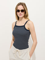 A woman stands against a white background with her hands in her pockets, wearing sunglasses, light beige drawstring pants, and the Lara Striped Tank in Fine Rib featuring navy blue and white '90s-inspired stripes with a square neckline.