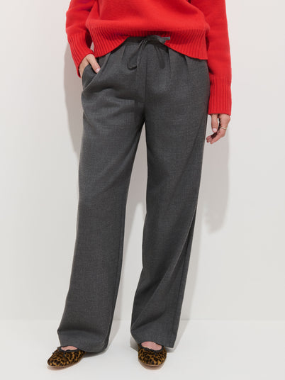 Person wearing a red sweater, the Hudson Pant in Wool Flannel featuring wide legs and a pull-on waist, and leopard-print flat shoes, standing against a plain light background.