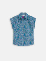 The Maddie Blouse in Liberty Cotton is a short-sleeve, button-up shirt with a blue and green floral pattern, made from Tana Lawn cotton by Liberty Fabric and finished with real shell buttons. Shown on a white background.