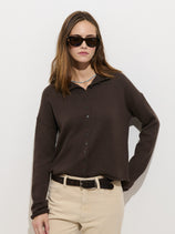 A person wearing a Taylor Cardigan in Cotton Cashmere, an oversized boxy sweater with dark brown Troca shell buttons, paired with tan trousers and sunglasses.