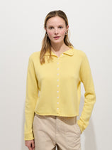 A woman with straight light brown hair wears the Taylor Cardigan In Cashmere in pale yellow and beige pants, standing against a plain white background with a neutral expression.