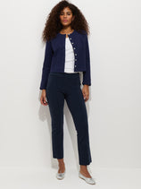A woman with curly hair stands confidently against a white background wearing the Cropped IYKYK Pant in navy, a white top, cardigan, and silver flats.