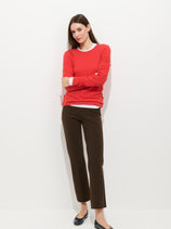 A woman with straight brown hair stands against a white background in a red long-sleeve top, black flats, and the Cropped IYKYK Pant. She crosses her arms and looks at the camera with a neutral expression.