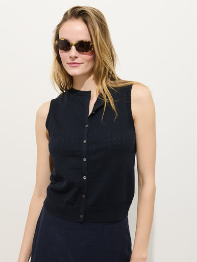 A woman in tortoiseshell sunglasses models the Odette Sweater Tank in Cotton Cashmere, a sleeveless dark navy button-up top, standing against a plain white background and looking off to the side with a relaxed expression.