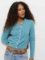 A person wearing a light blue extrafine merino Elizabeth Street Cardigan in Merino Wool with white buttons, paired with blue jeans and a brown leather belt.